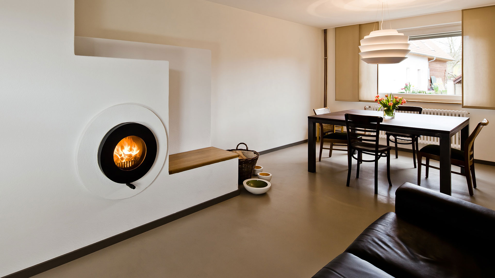 Schwarzer firetube Ofen mit sichtbarem Feuer, in eine weiße Wand integriert; im Hintergrund ein Esstisch.