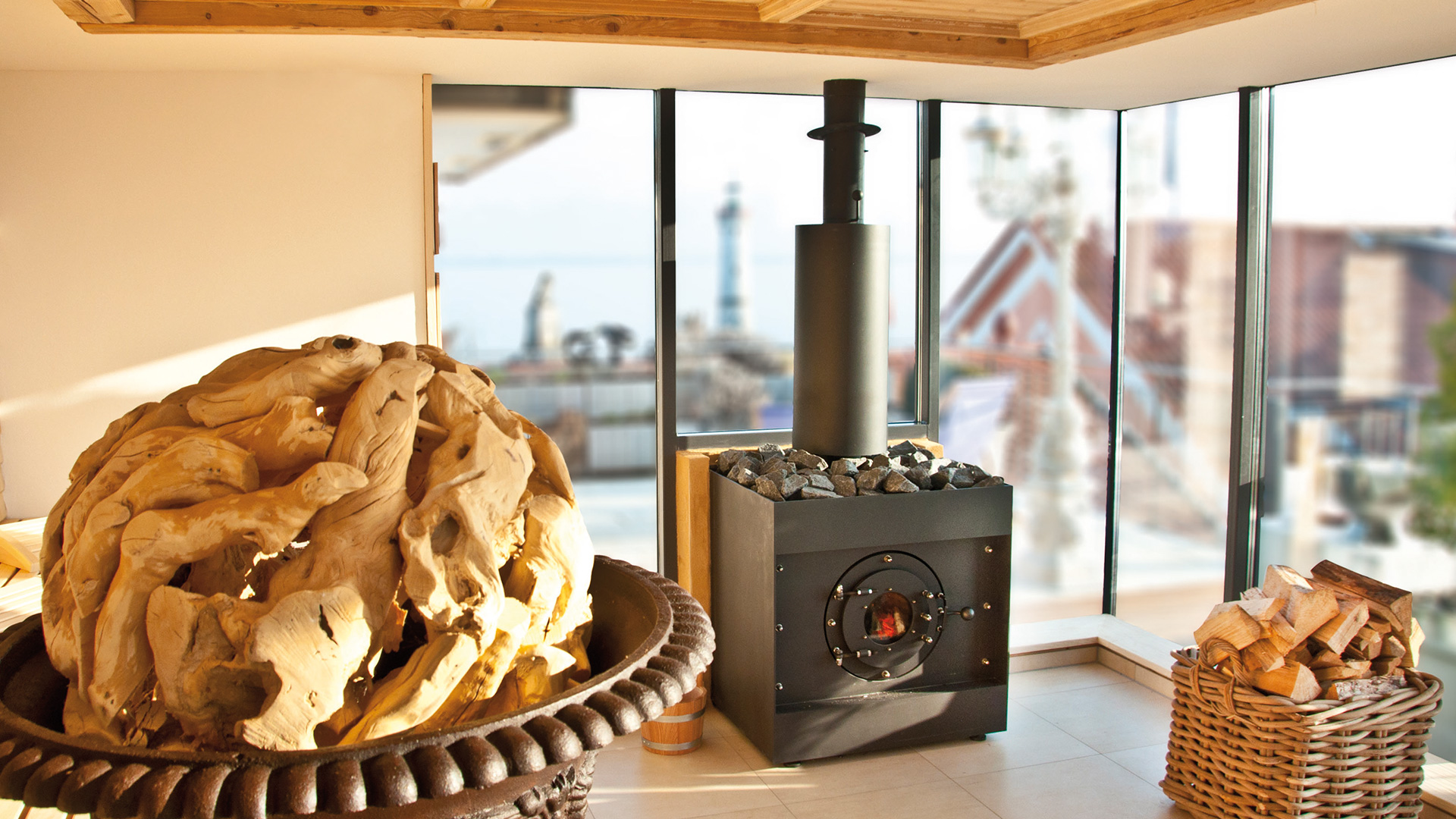 firetube Saunaofen in Sauna mit Glaswand, davor Holzdekoration und Korb mit Holzscheiten auf dem Boden.