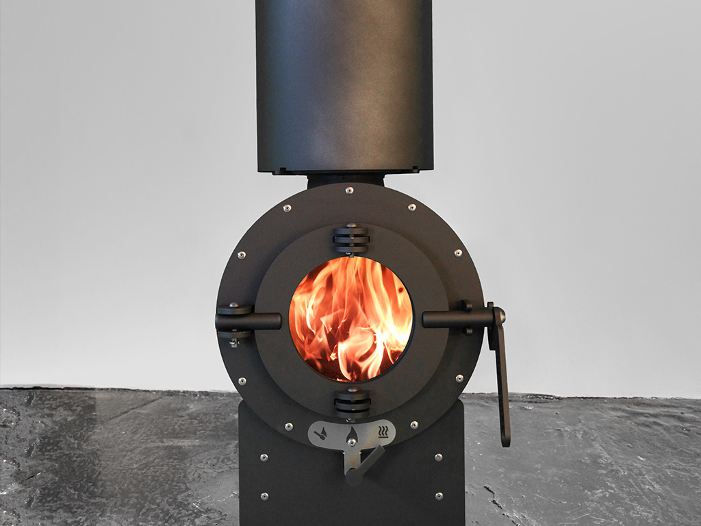 Schwarzer firetube Ofen in Frontalansicht mit sichtbarem Feuer; schwarzer Boden und weiße Wand im Hintergrund.